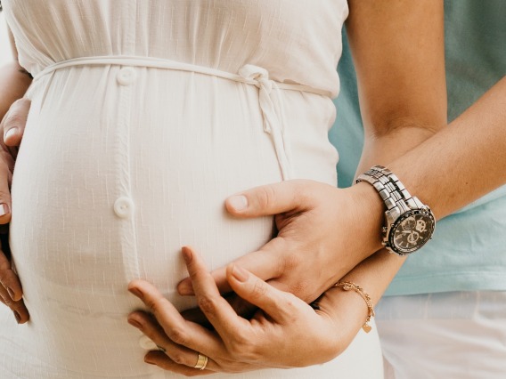 Crop pregnant woman embracing tummy with husband