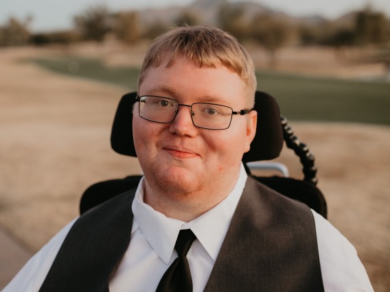 White man with glasses wearing a suit vest and tie, sitting in a wheelchair