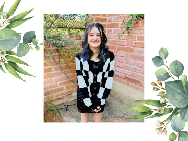 Tessa, standing outside on a sunny day wearing a black and white checkered coat and her signature smile