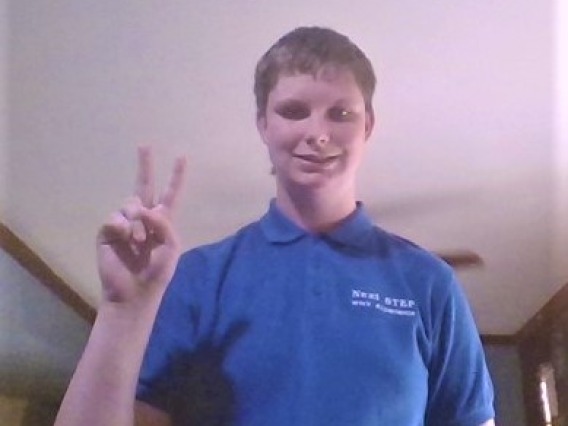 Lexi Dibbern, a white teenager with short hair in a blue polo shirt doing the "peace" sign