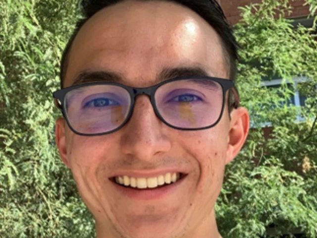 Nick Marcell, Sonoran Center trainee, smiling in front of some trees