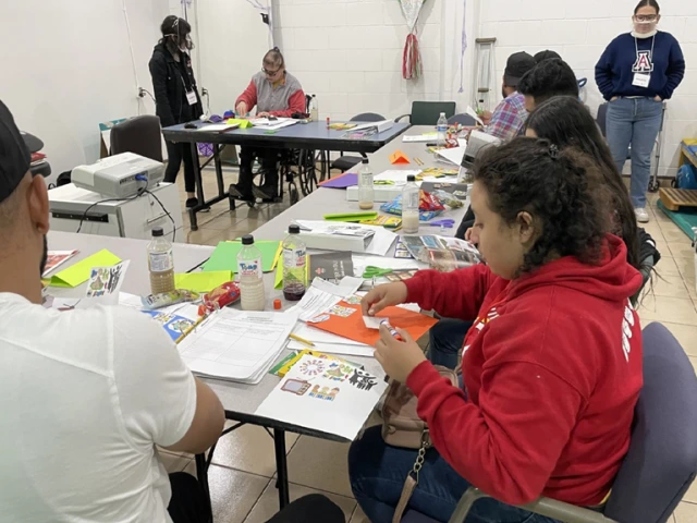 Participants in the DISCAPAZ scrapbooking workshop work on their creations, while Paulette Nevarez stands in the background, observing