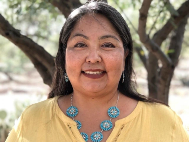 Native woman with long dark hair wearing a yellow blouse and turquoise necklace