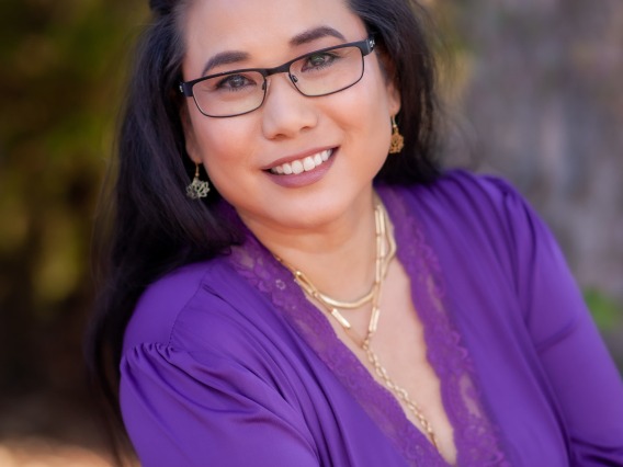 Woman with long dark hair and glasses wearing a purple blouse