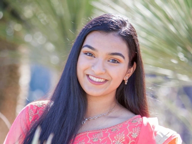Freya Abraham, a young person with long brown hair, outside, smiling, wearing a pink-orange top