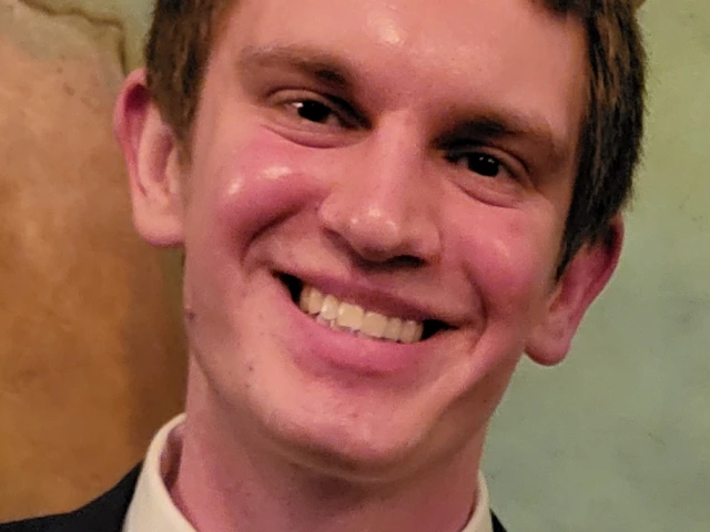 Drew Milne,  a white man in his late 20s with short brown hair, wearing a suit with a white shirt, copper tie, and blue jacket