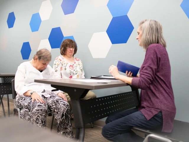 Three older adults sitting around a table in a classroom setting