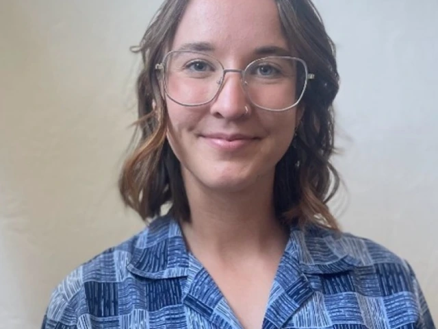 Audrey Beermann, a young person with long brown hair, wearing glasses and a blue flannel shirt