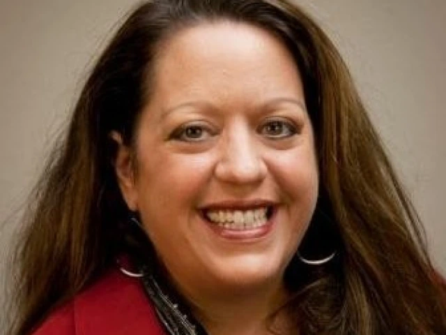 woman with long brown hair, wearing a red blouse and is smiling at the camera
