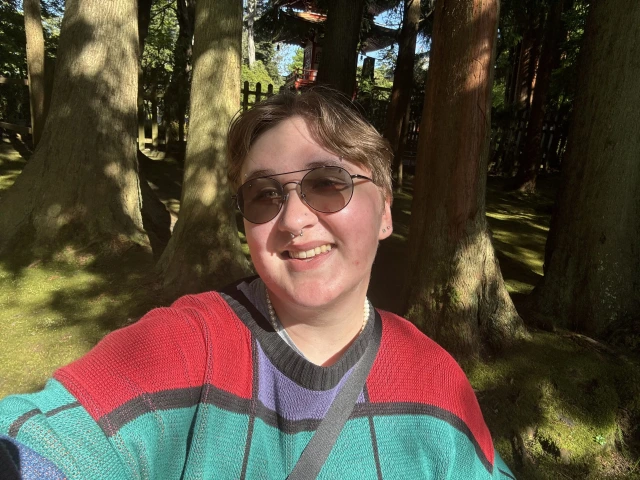 photo with person wearing sunglasses and has on a blue and red seater and is smiling at the camera