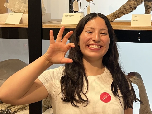 photo of young adult with long brown hair, wearing a white shirt and is smiling at the camera