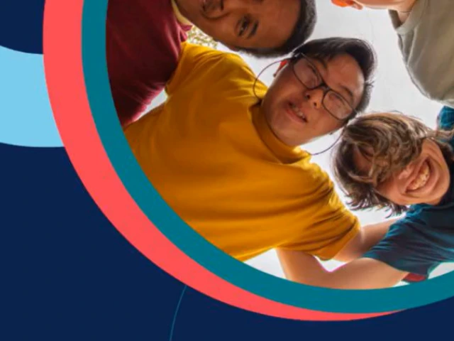 A group of 4 boys huddled in a circle looking at the ground smiling. 