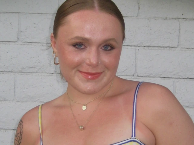 photo of young adult with a yellow spaghetti strap shirt, has brunette hair pulled back into a bun and is smiling at the camera