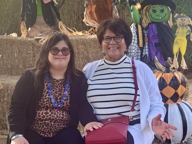 Francine (left) and her mother, Maria (right), sitting outside on a hay bale surrounded by Halloween decorations