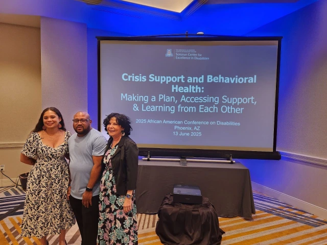 Jacy Farkas, David Taylor, and Barbara Brent smile in front of the title slide to their presentation, Crisis and Behavioral Health: Making a Plan and Accessing Support, Learning from Each Other