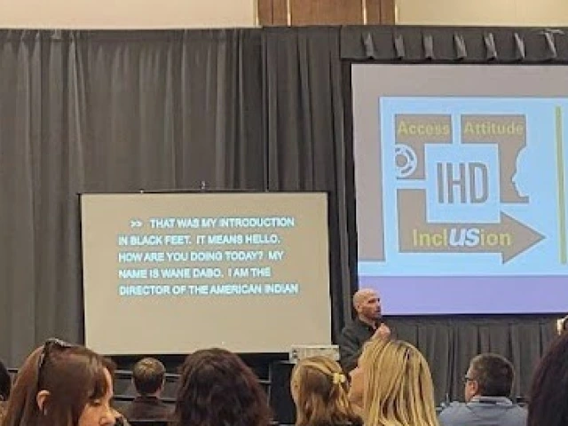 A man speaking at a podium next to a screen showing the IHD Evidence for Success Conference logo.