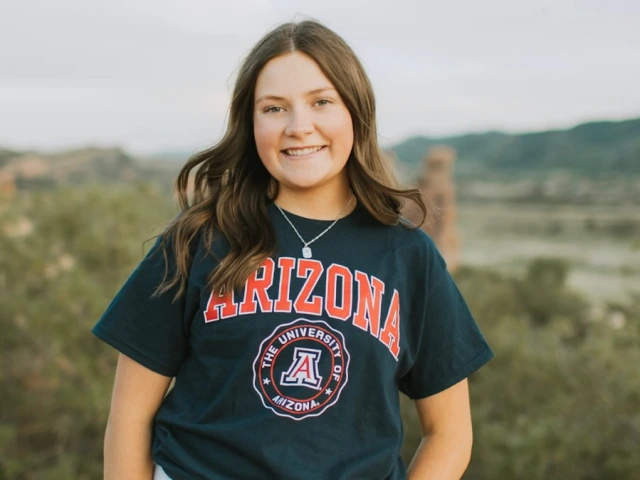 young woman wearing a blue U of A shirt and is smiling at the camera with a mountains background