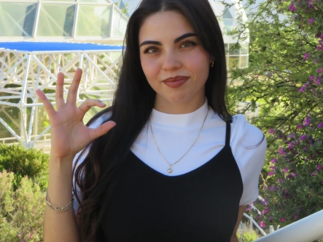 Alehxia Apodaca, a young person with long dark hair, wearing a black top over a white shirt, in front of a glass building