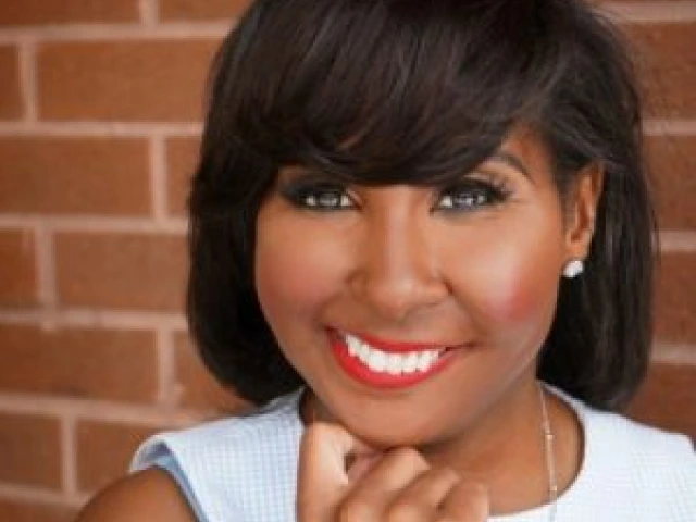 Black woman with medium-dark brown hair. She is wearing a sleeveless blue and white checkered top, with a silver necklace, wearing red lipstick smiling.