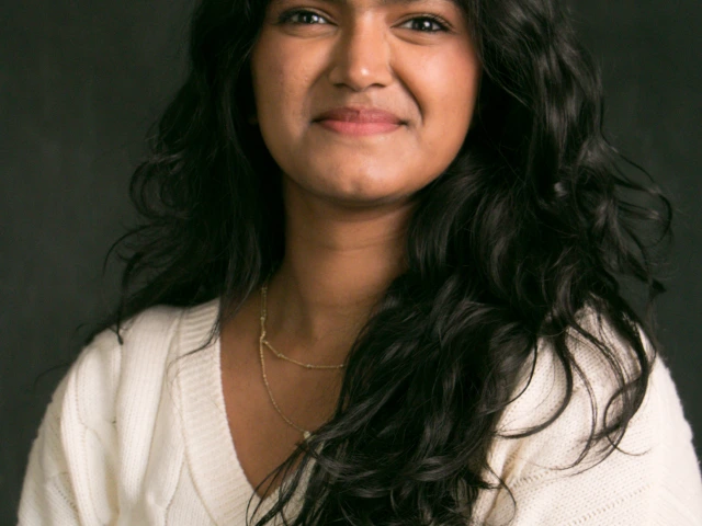 A dark background with the person in question smiling wearing a white sweater