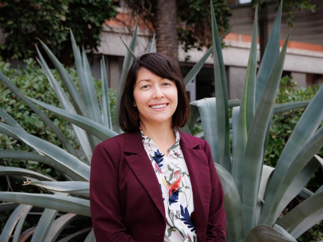 woman wearing a burgundy blazer, has short brown hair and is smiling at the camera