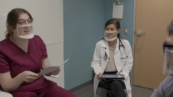 Image of two young healthcare professionals speaking to an young man with a disability.