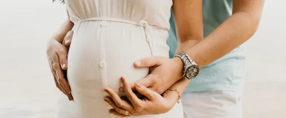 Crop pregnant woman embracing tummy with husband