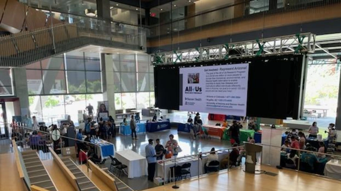 A wide-angle photo of the event, showing groups of people gathered around information tables.