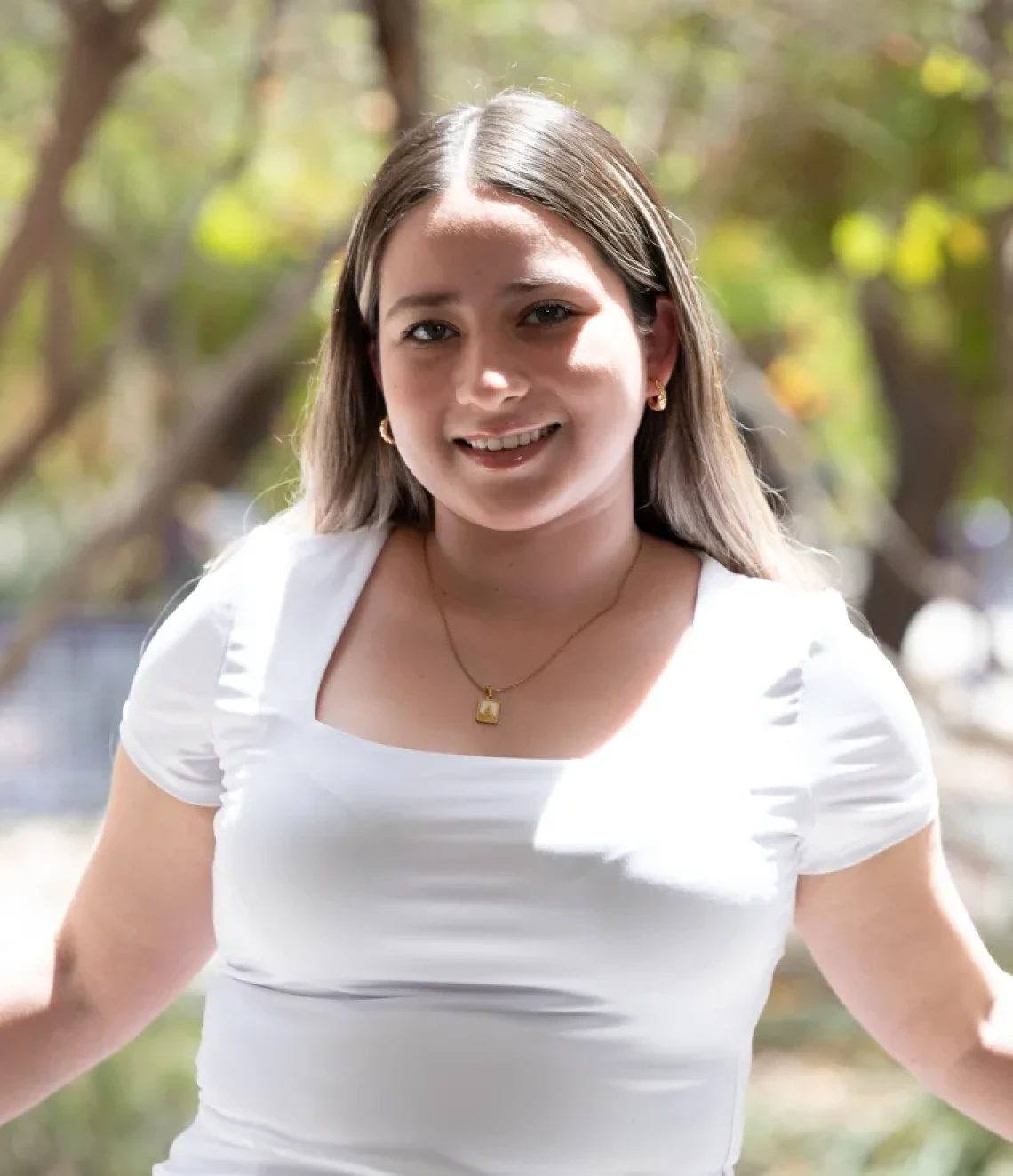 Ana Fernandez, a woman with light skin and blonde hair, wearing a white top, standing outside near some trees