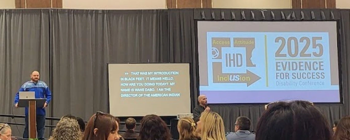 A man speaking at a podium next to a screen showing the IHD Evidence for Success Conference logo.