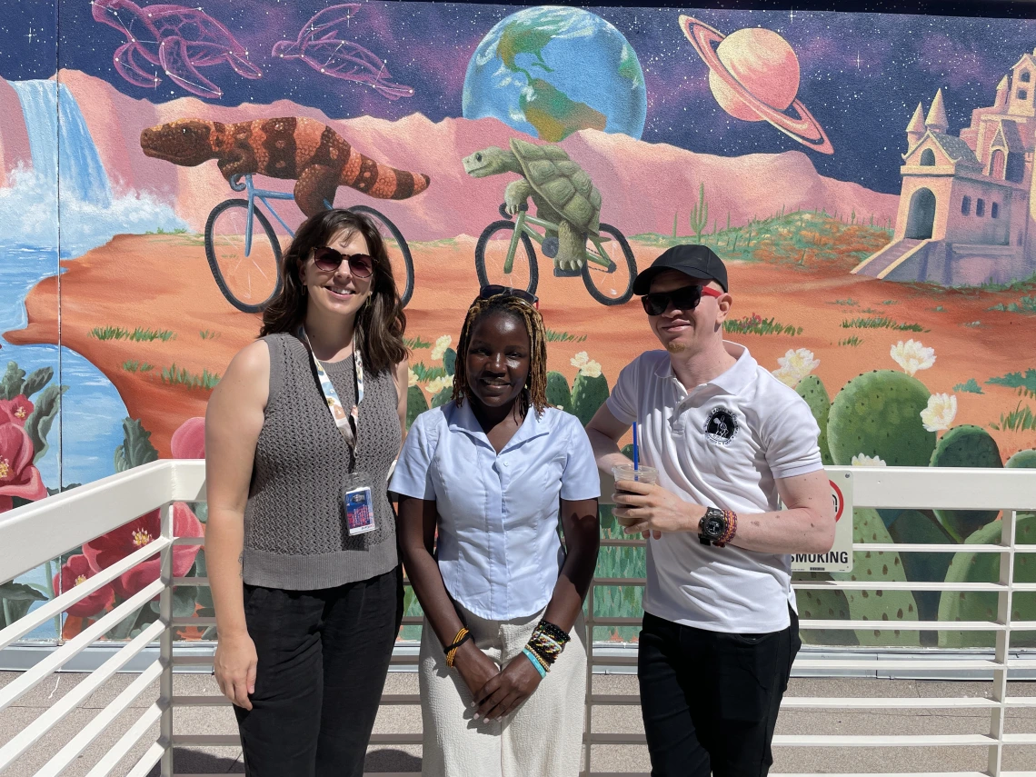 Mai Nambooze and Kelvin Mkude standing with Loretta Alvarez in front of a Sonoran Desert-themed mural