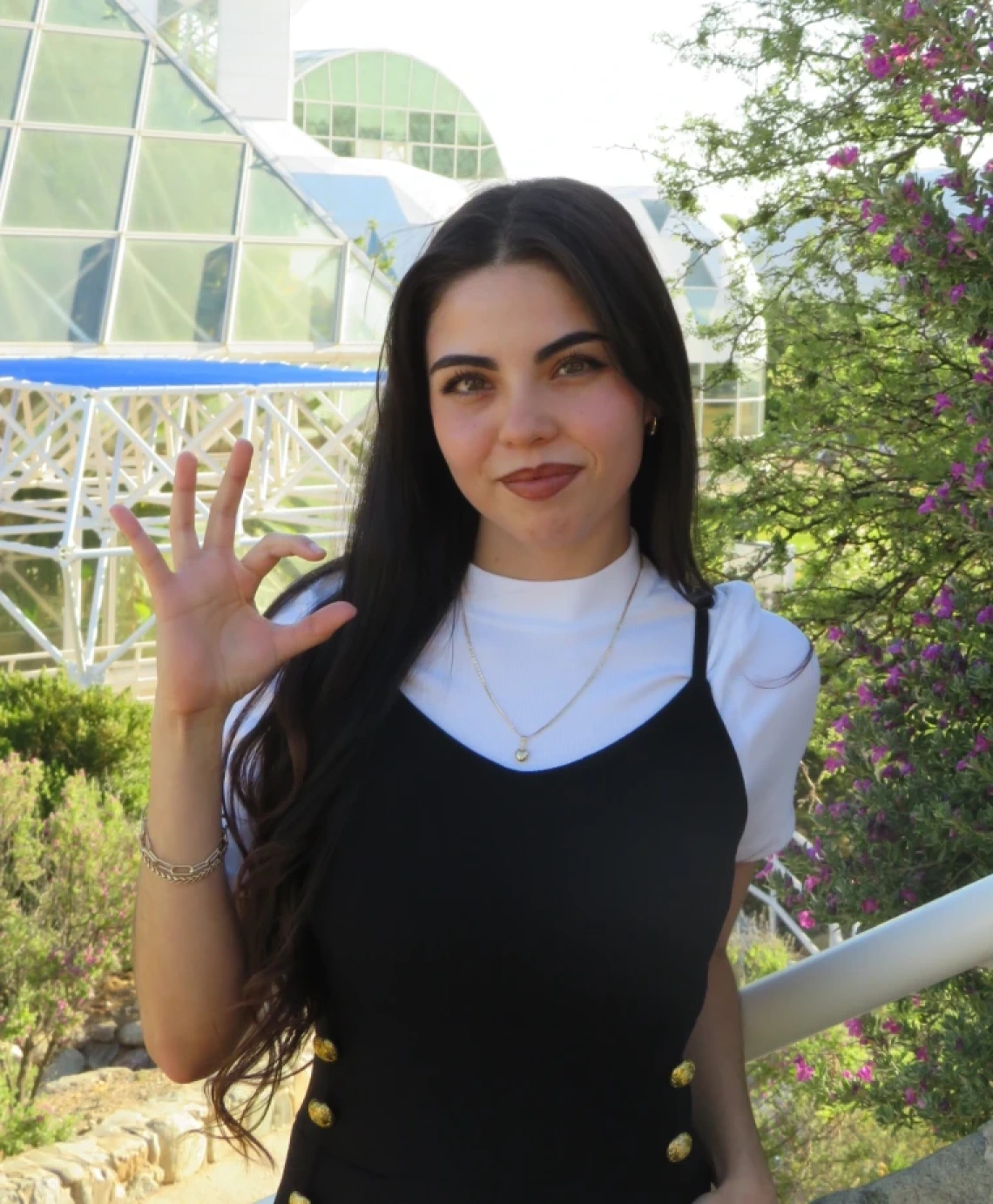 Alehxia Apodaca, a young person with long dark hair, wearing a black top over a white shirt, in front of a glass building