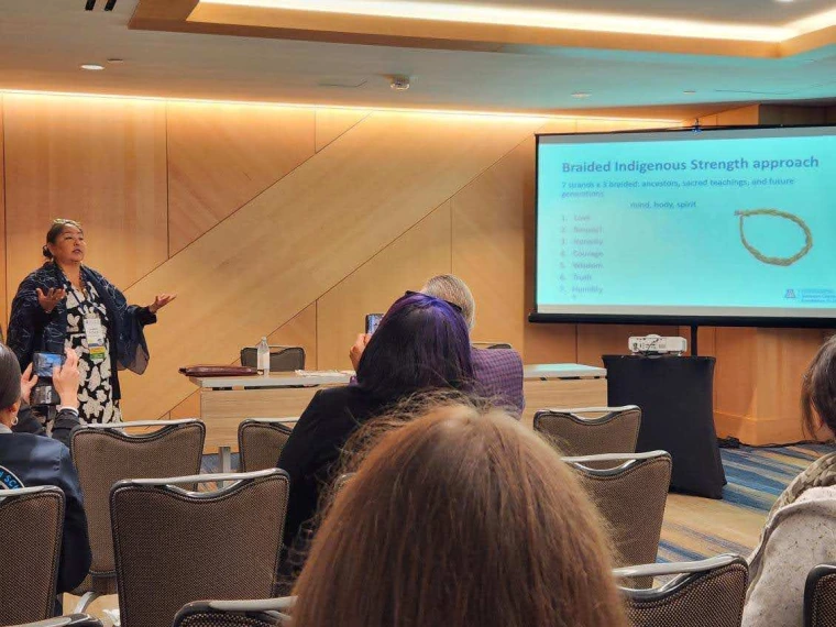 Agnes Attakai delivering a powerpoint presentation in front of a seated audience.