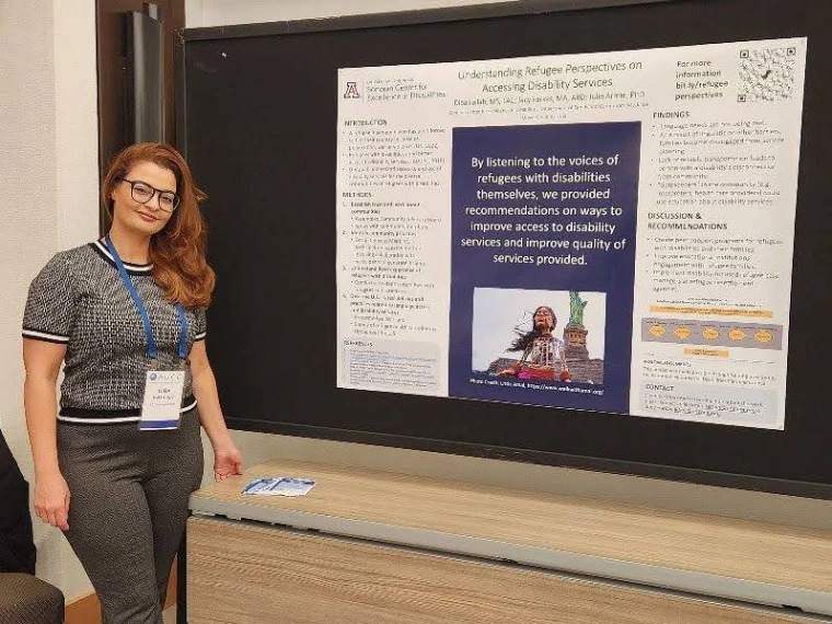 Diba Fallah standing next to her poster and looking into the camera