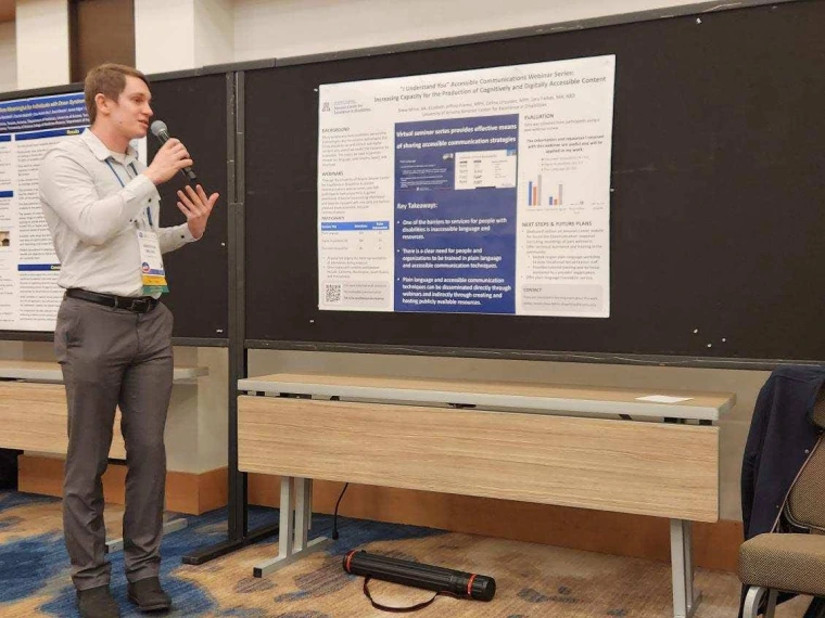 Drew Milne presents his poster, looking towards the poster and gesturing to it.