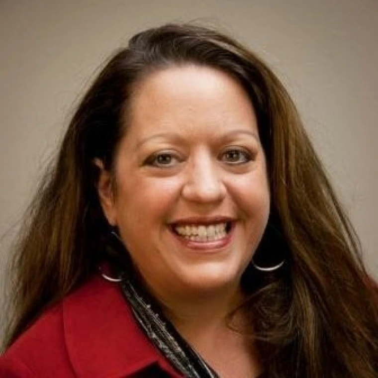 woman with long brown hair, wearing a red blouse and is smiling at the camera