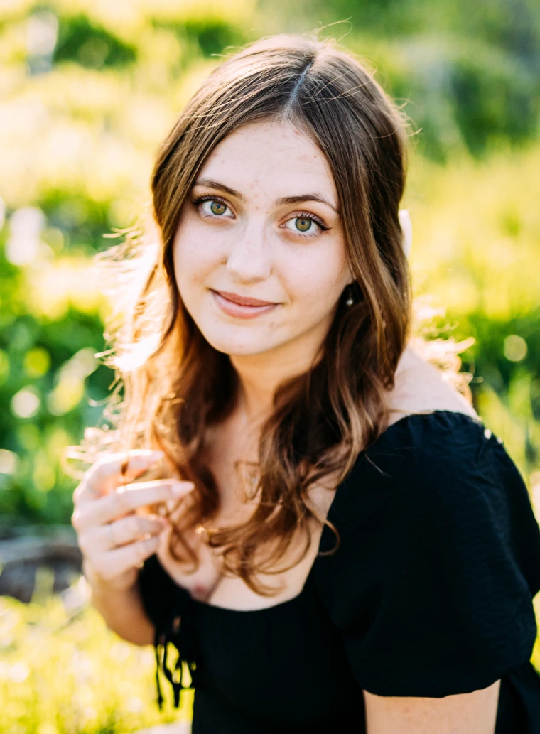 photo of young woman with a black dress, she has shoulder length brunette hair
