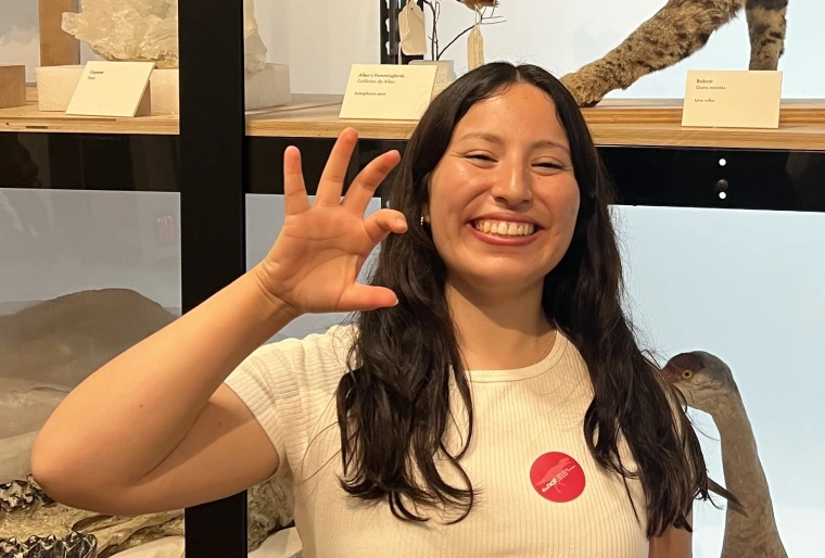 photo of young adult with long brown hair, wearing a white shirt and is smiling at the camera