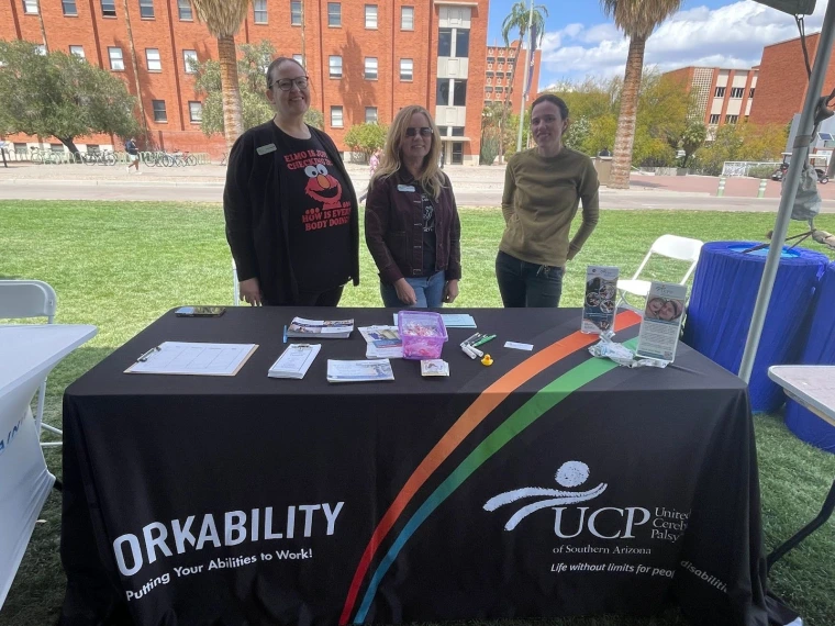 WorkAbility representatives standing behind their table. Their table has fliers, brochures, and a sign-up sheet.