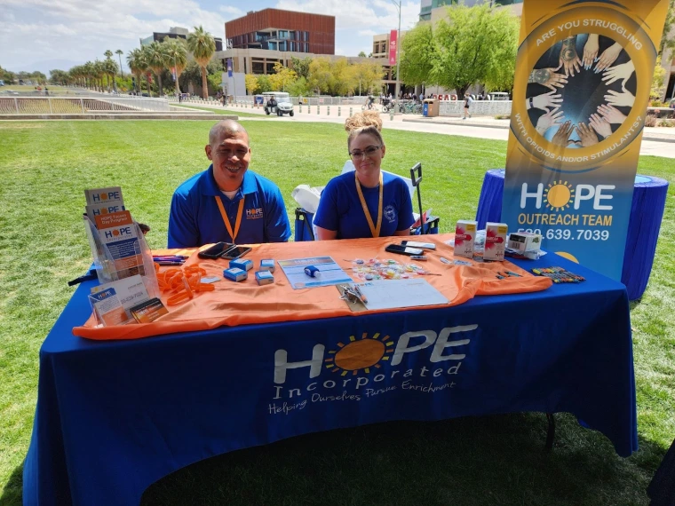 Hope Incorporated representatives sitting at their table. The table has a sign up sheet and various brochures. 