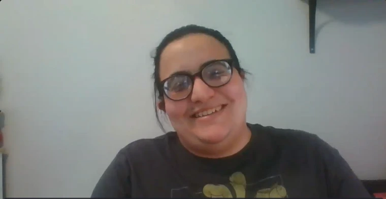 Audra Paletta leads a role-play scenario about self-advocacy in the workplace. They are wearing glasses and a t-shirt, and smiling in an indoor setting