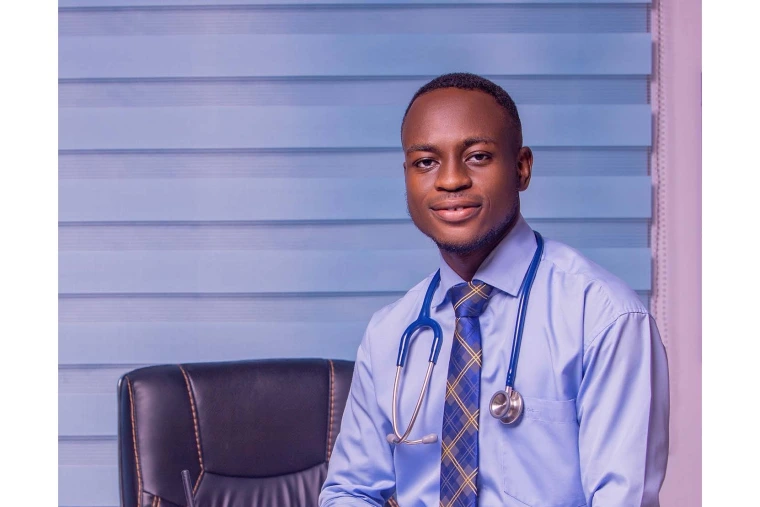headshot of young man wearing a blue collard shirt, checkered tie, and with a stethoscope around his neck