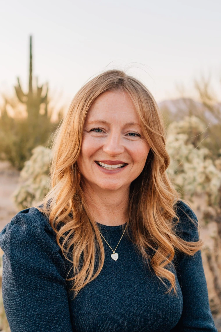 Woman wearing a navy blue shirt, has long strawberry blonde hair and she is smiling at the camera