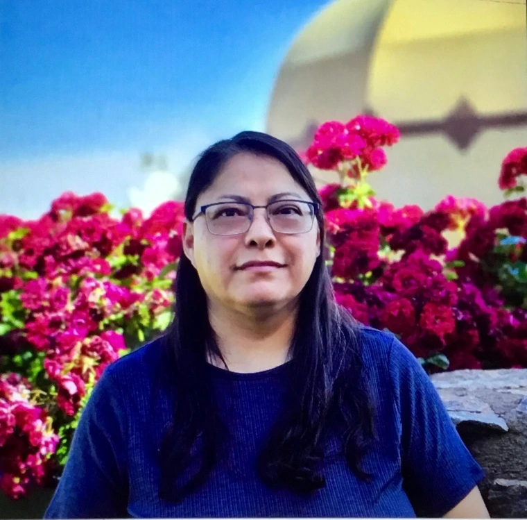 woman with long black hair, wearing glasses and is smiling at the camera