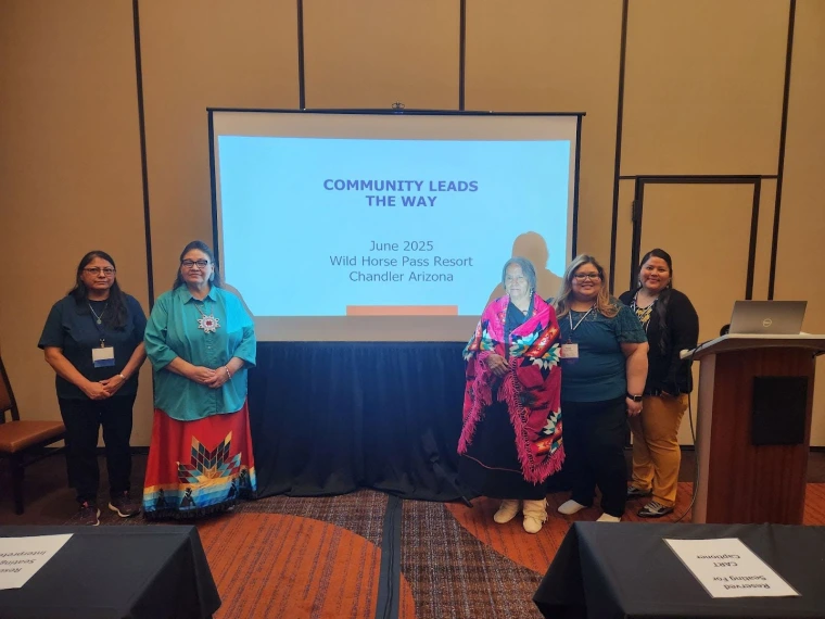 Rosa Rojas-Franco and colleagues pose next to the title slide of their presentation, "community leads the way"