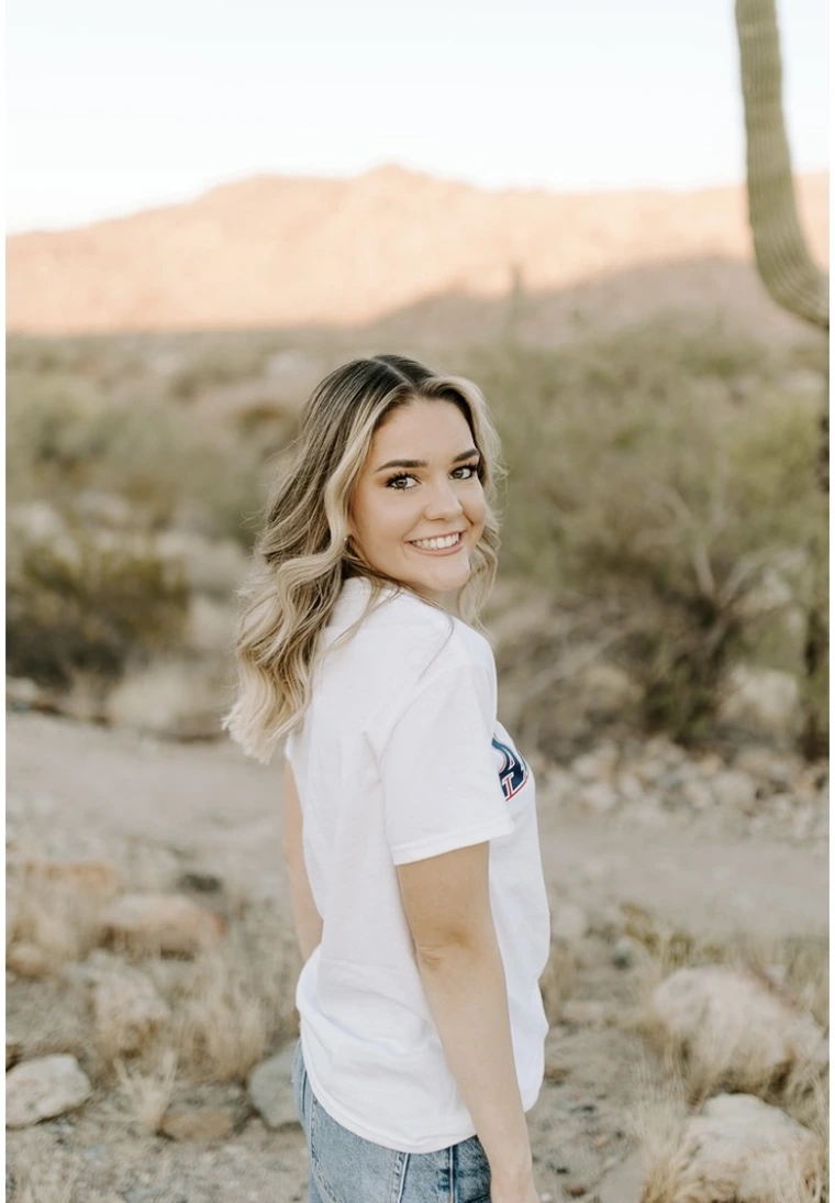 young woman wearing a white t-shirt, has medium length hair and standing in front of a desert background