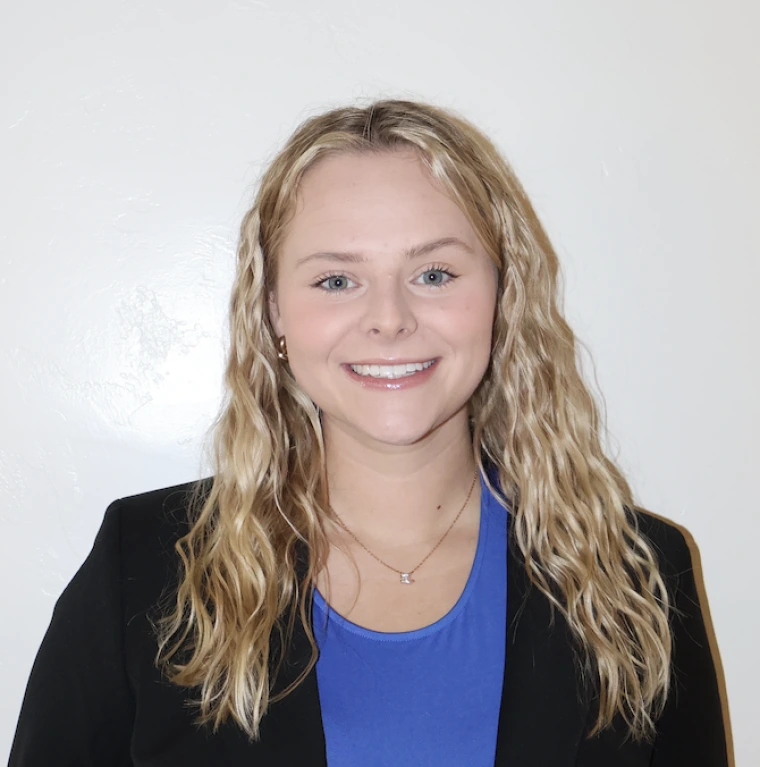 photo of young woman wearing a blue shirt and black blazer, she has blonde wavy hair and is smiling at the camera