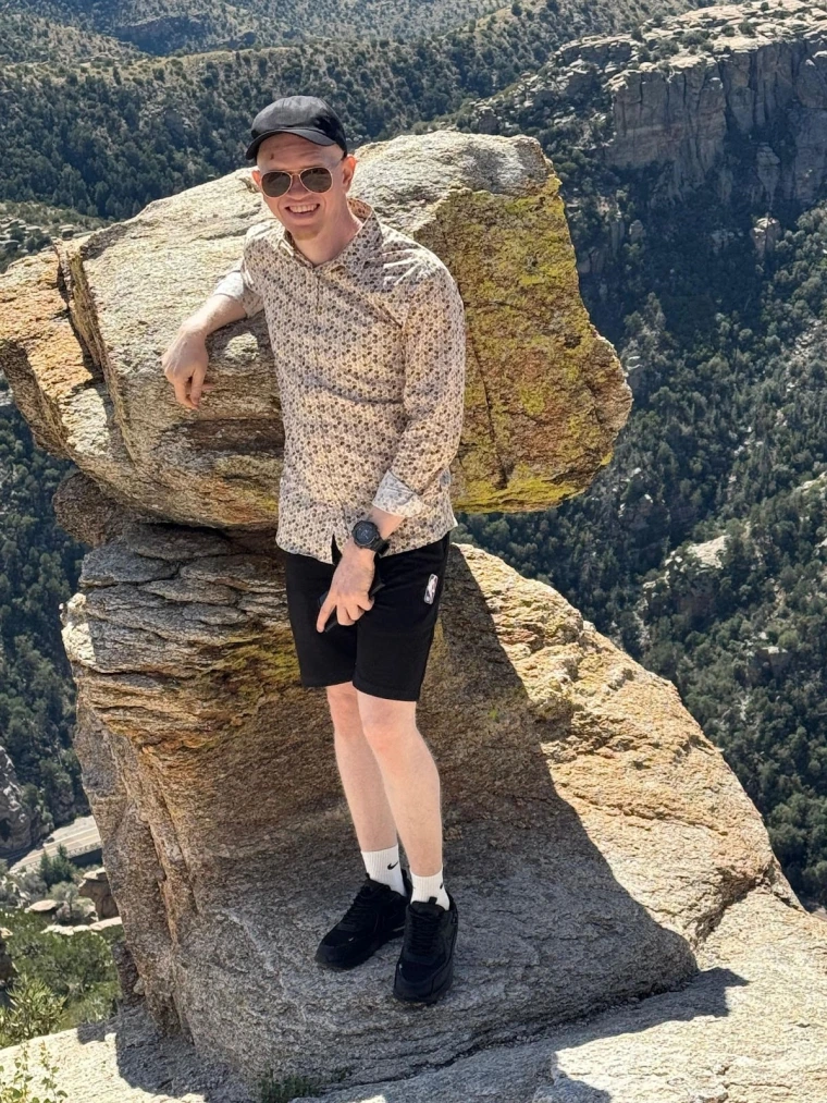Kelvin poses for a photo in front of a large rock at the summit of Mount Lemmon