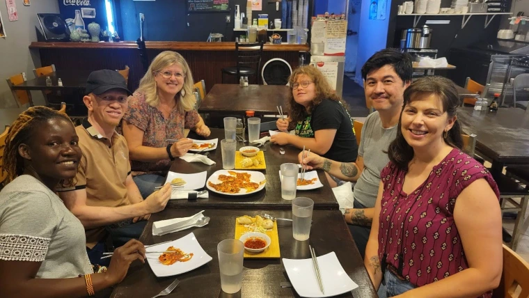 Mai, Kelvin, and Loretta sitting around a dining room table having dinner with Loretta's family