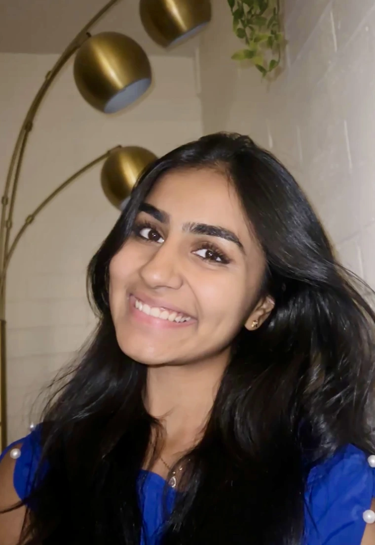 Srishti Rajeev in Blue Shirt against white wall, she is smiling at the camera